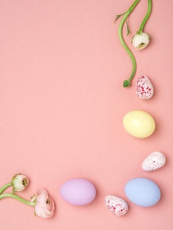 Elegant minimalist Easter Holiday frame. Yellow, blue and violet eggs near tender pink ranunculuses on peach pink background. Top view, space for text.の写真素材