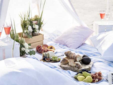 Summer brunch or dinner organized on a sea shore for friends. Elegant decorated place for romantic date. Flowers, fruits, cheese and bread as a light snacks for summer camping or picnic. Outdoor party celebration idea.の写真素材