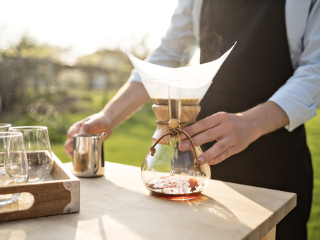 Male hands holding drip coffee utensil. Barista preparing filter coffee outdoor. Coffee catering. Alternative coffee brewing.の写真素材
