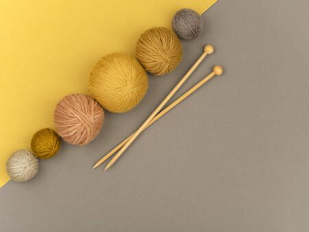 Row of woolen  various colored balls of yarn and wooden knitting needles on gray and yellow background. Craft, knitting or hand made concept. Winter hobby background. Top view, flat lay. Horizontal image.の写真素材