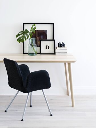Minimalist workspace for hipsters. Light clean room. Black chair, wooden table with books, posters, camera and tropical plant's leaf.の写真素材