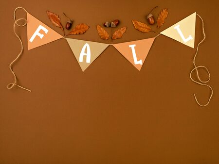 Fall lettering on cardboard. Top view of greeting paper garland with acorns and oak leaves on dark brown background. Autumn theme border, frame.の写真素材