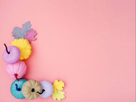 Creative corner border of various colorful pumpkins on a pink background. Bright hand-dyed pumpkins and oak leaves. Autumn Thanksgiving background. Flat lay with space for text.の写真素材