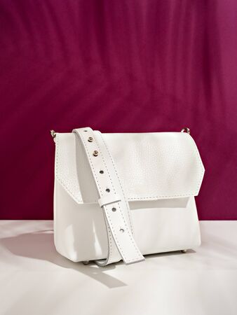 Minimalist stylish female accessory. Trendy white cross body handbag on an deep pink background covered with tropic leaves shadow. Summer sale, style, fashion, female accessories or creative outfit concept. Copy space for text.の写真素材