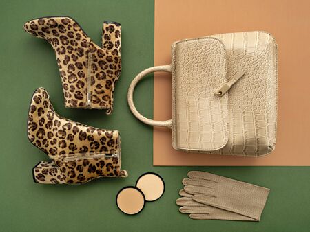 Top view on a pair of trendy leopard print boots, crocodile crossbody bag, leather gloves, and makeup products. Flat lay of feminine trendy accessories in green and beige tones.の写真素材