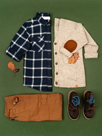 Kids autumn apparel. Toddler boy plaid shirt, cargo pants, sweater and boots on forest-green background. Kids boutique clothing. Thanksgiving day and fall concept. Flat lay, top view.の写真素材
