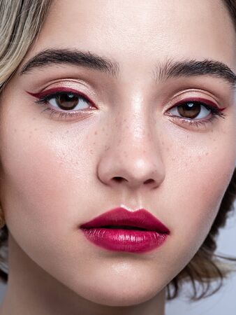 Close up portrait of a pretty girl with freckles, glowing fresh skin and wavy hairs. Young pretty model with bright make-up on gray background. Feminine beauty. Eye makeup, eyeliner.の写真素材