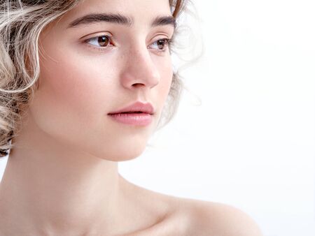 Close up portrait of a cute young girl in a soft daylight . Charming model with bare shoulders, clean fresh skin and cute curls on white background. Natural feminine beauty. Natural make-up.の写真素材