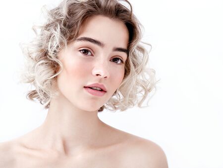 Portrait of a cute young girl with bare shoulders, clean fresh skin and cute curls. Charming caucasian model with natural make-up on white background. Natural feminine beauty. Soft daylight.の写真素材