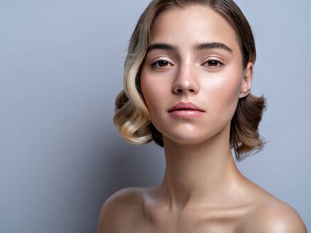 Closeup beauty portrait of a model with natural shiny makeup. Bare shoulders, wavy hairs and trendy highlighter on skin. Cosmetics and make up. Horizontal image.の写真素材