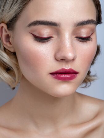 Close up portrait of a pretty young girl with red eyeliner, glowing fresh skin and wavy hairs on gray background. Natural feminine beauty. Eye makeup.の写真素材