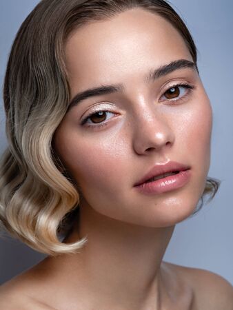 Closeup beauty portrait of a model with natural shiny makeup. Bare shoulders, wavy hairs and trendy highlighter on skin. Cosmetics and make up. Vertical image.の写真素材
