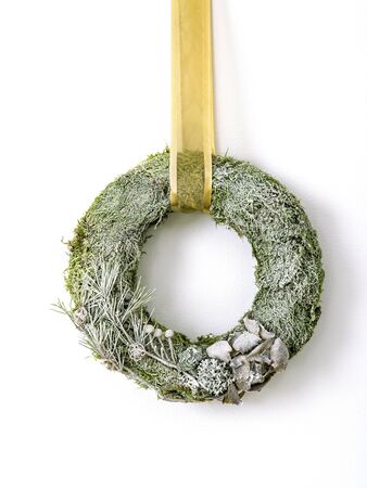 A hand crafted Christmas wreath featuring frosted foliage, moss and needles. Wreath hangs against a wall, finished with a ribbon. Get into the festive season with a Christmas beautiful decoration.の写真素材
