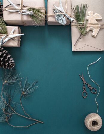 Top view of gifts wrapped in a craft paper and decorated with artificial deer horns, hemp cord and needles. Christmas themed frame with hemp rope ball, scissors, pine cones and branches.の写真素材