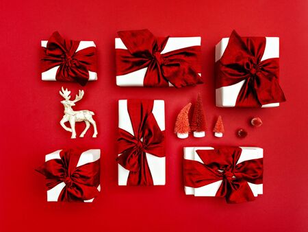 Top view of Christmas gift boxes laid out on a red background. Composition of gifts with red bows and ribbons, deer and artificial red fir-trees.の写真素材