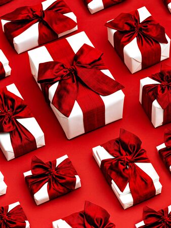 Top view on white gift boxes laid in rows on a red background. Background made of gifts wrapped in white craft paper and decorated with red bows and ribbons.の写真素材