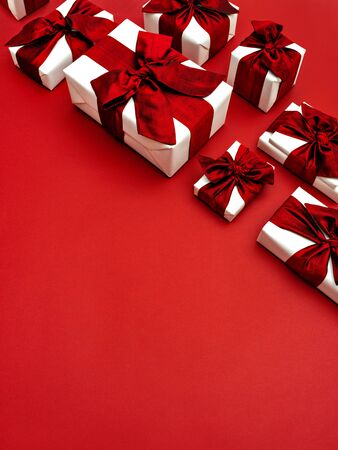 Top view on Christmas gift boxes laid in rows on a red background. Top right corner border or frame made of gifts with red bows and ribbons. Flat lay, copy space for text.の写真素材