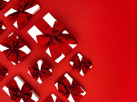 Top view on Christmas gift boxes laid in rows on a red background. Bottom left corner border or frame made of gifts with red bows and ribbons. Flat lay, copy space for text.の写真素材