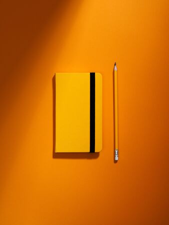 Notebook and pencil minimalist flat lay. Starting and preparing for the new year concept. Planner for new year or year results. Writer equipment on orange background. Top view, space for text.の写真素材