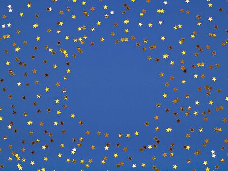 Classic blue background covered with golden stars sequins. Top view. Copy space for text. Christmas time frame. Concept of winter holiday.の写真素材