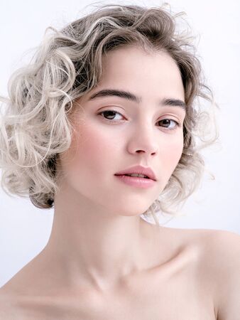 Portrait of a cute young girl with bare shoulders, clean fresh skin and cute curls. Charming caucasian model with no make-up on white background. Natural feminine beauty. Soft daylight.の写真素材