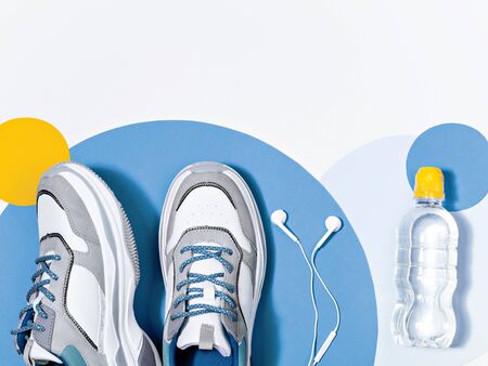 Trendy blue toned composition of a sport shoes, bottle of water and earphones on the colourful confetti background. Reducing weight, getting fit and healthy life style idea. Sport themed frame.の写真素材