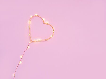 Warm glowing electric garland shaped as a heart on pink background. Sant Valentines day concept. Greeting card, invitation.  Top view, copy space for text.の写真素材