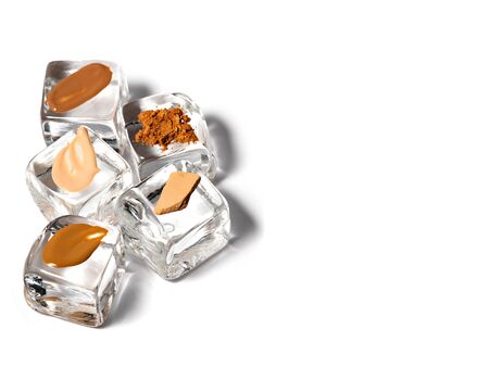 Samples of different tones of liquid foundation, concealer, shimmer, powder on artificial ice cubes isolated on white background.Iced face makeup, cooling cosmetics concept.の写真素材