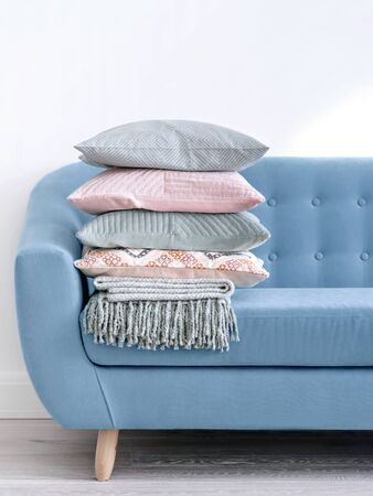 Trendy denim blue sofa decorated with pale of cushions and woollen plaid in bright sunlit room with minimal design. Living Room concept.の写真素材