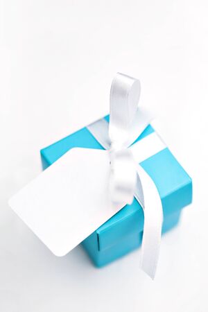 Top angled view of turquoise blue gift box decorated with white satin ribbon and blank tag over white background. Single surprise gift box. Presents, celebration, Sant Valentine's theme. Copy space.の写真素材