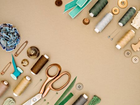 Frame with sewing tools in earthy beige and green colours. Dressmaking conceptual background. Sewing threads, needles, pins, scissors, buttons and ribbons. Top view, flat lay design for tailor's business.の写真素材
