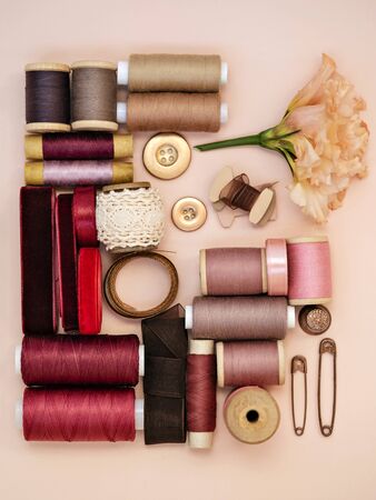 Top view of sewing supplies as various ribbons, bobbin, pins on pinkの写真素材