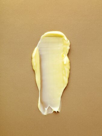 Smear of yellow face or body cream texture on gold shimmering background. A sample of a body treatment cosmetic product. Cosmetology concept.の写真素材