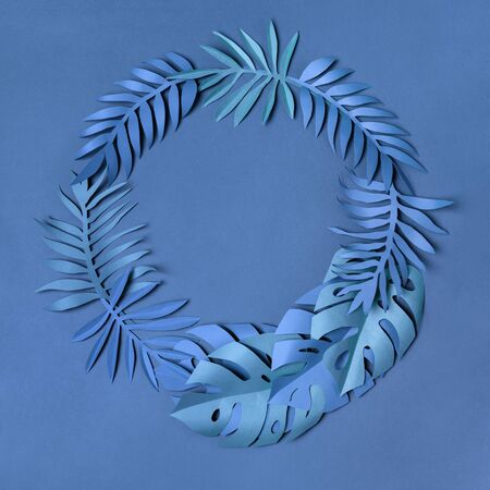 Studio shot of nice wreath composed of blue paper cut tropical leaves on classic blue background. Botanical background. Summer vibes. Flat lay.の写真素材