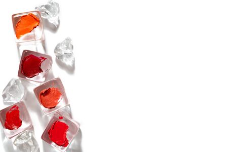 Creative image of red and orange lipstick samples. Lipstick strokes on artificial ice cubes isolated on white background. Cooling cosmetic products arranged in random order. Summer makeup concept.の写真素材