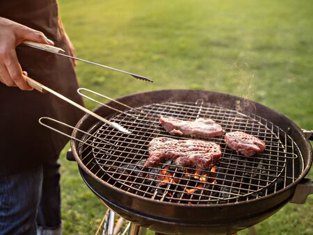 Background with back light representing outdoor cooking, summer gathering, BBQ, grill party in the garden. . Unrecognisable man near grill trolley cooks meat. Shallow depth of field.の写真素材