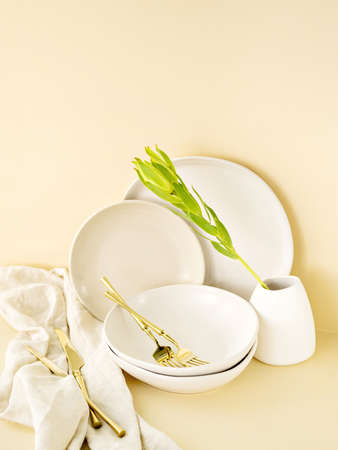 Minimalist set of empty crockery in natural day light with golden cutlery. Beige and earthy colours. Handmade ceramic, pottery, restaurant or catering concept. Copy space.の写真素材