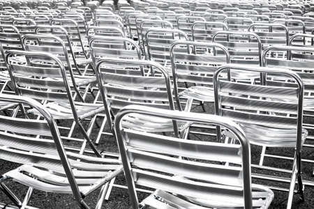 Shiny metallic chairs in rows prepared for public event. Empty seats in public space.Abstract urban background. Rhythms and perspective, high contrast image.の写真素材