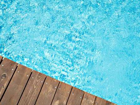 Ripped wavy water surface in swimming pool with wooden, old deck. Top view of swimming pool area in hotel or villa. Summer vacation simple background.の写真素材