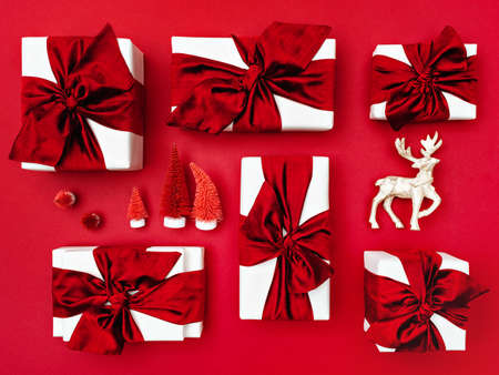 Top view of Christmas gift boxes laid out on a red background. Composition of gifts with red bows and ribbons, deer and artificial red fir-trees.の写真素材