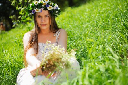 Portrait of a girl with circlet of flowers. She is sitting in a green meadowの写真素材
