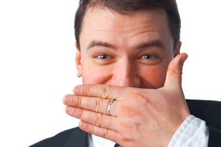 Close up portrait of young smiling businessman covering mouth with his hand while looking at you over white の写真素材