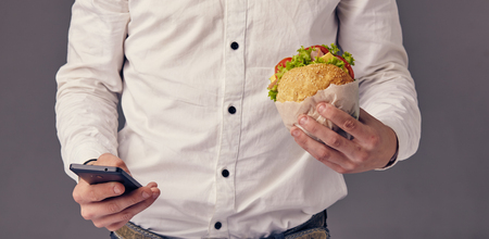 man eat hamburger in cafe while watch video on his phoneの写真素材