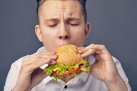 Young man eating a fresh burgerの写真素材