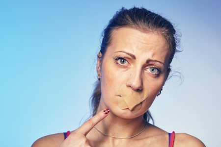 Young woman with his mouth glued with tape.の写真素材