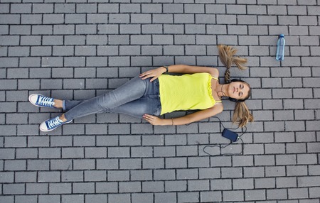 Young woman in a T-shirt with listening music and lies on the pavement
