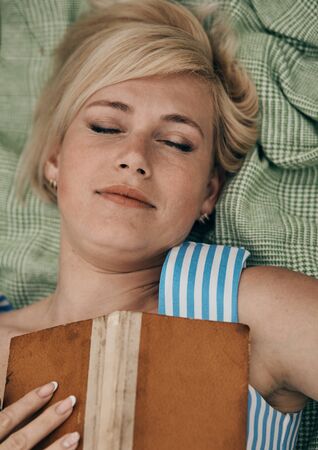 Woman lying on plaid in field and enjoying reading books.