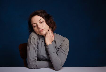 young worried woman. She sits at a table against on a dark blue background