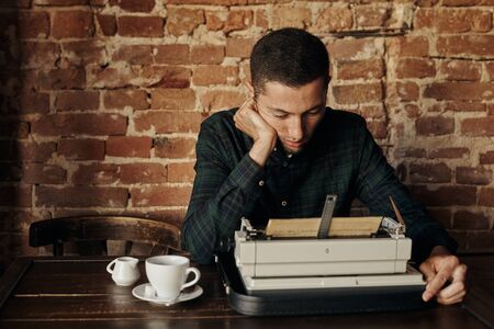 Young man writing on an old typewriter. He ponderedの写真素材