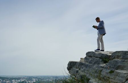 businessman stands on a rock and looks at his tablet
